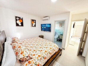 Quarto com uma cama, uma televisão e uma porta que dá para um banheiro.
