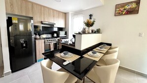 A modern kitchen with a black refrigerator, stove, microwave, and a dining area with a black table and four chairs. - Perfect 2-bedroom building with AC in welcoming Punta Cana (Punta Cana)