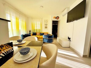 Uma sala de estar moderna com sofá, mesa de jantar, cadeiras e TV fixada na parede.