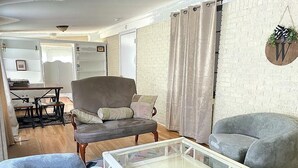 A living room with a sofa, two armchairs, a glass coffee table, and a brick wall. - Quintessential cottage walking distance to Oaklawn and minutes from downtown (Hot Springs)