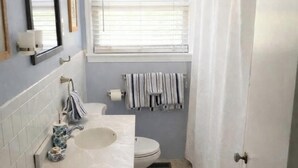 A bathroom with a white sink, toilet, and shower curtain. - Quintessential cottage walking distance to Oaklawn and minutes from downtown (Hot Springs)
