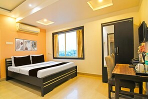A hotel room with a bed, a window with curtains, a desk with a chair, and a television. - Deluxehotel O Baguiati Formerly GR (Barasat)