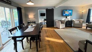 A spacious living room with a dining area, a flat-screen TV, and a large window.
