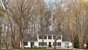 A two-story white house with a dark roof, surrounded by trees and a well-maintained lawn.