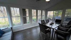 A sunroom with a dining table and chairs, large windows, and a ceiling fan.