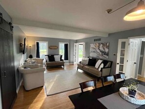 A spacious living area with a sofa set, a dining table, and a kitchen area with a refrigerator. - Wooded Lakeside Retreat Near Grand Park + GameRoom (Arcadia)