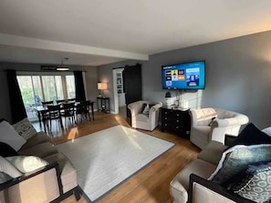 A modern living room with a flat-screen TV, two sofas, a coffee table, and a dining area with chairs and a table.