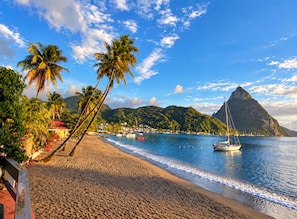 A beach with palm trees, a sailboat, and a mountain in the background. - Ma G’s Downtown Soufrière Townhouse (Soufriere)