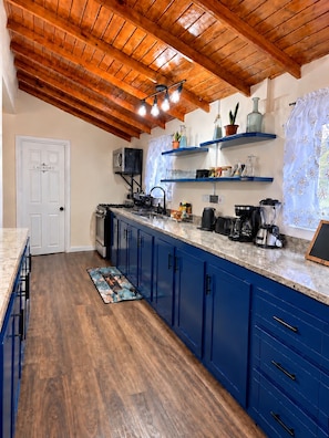 A kitchen with a wooden ceiling, blue cabinets, a marble countertop, and various appliances. - Ma G’s Downtown Soufrière Townhouse (Soufriere)