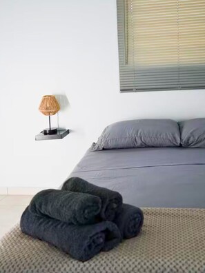 Une chambre à coucher avec un lit, des oreillers, une lampe et une couverture enroulée sur un tapis.