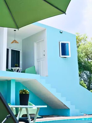 Un bâtiment moderne à la façade bleue, un escalier menant à un balcon, une petite table avec une chaise et une plante en pot.