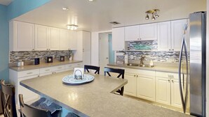 Una cucina moderna con pensili e basi bianche, un'isola centrale e un frigorifero in acciaio inossidabile.