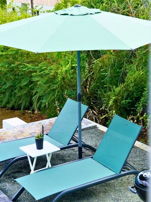 Eine Terrasse mit zwei grünen Lounge-Stühlen und einem kleinen Tisch, umgeben von Pflanzen.