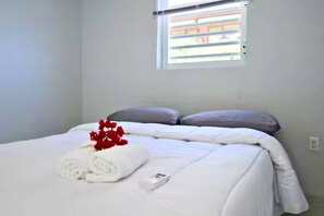 Ein Schlafzimmer mit einem Bett, Kissen, einem Fenster und einer roten Blumenkomposition.