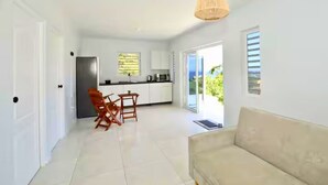 A modern kitchen with white cabinets, a dining area with a table and chairs, and a large window offering a view of greenery. - Westpunt Villa  l 2BR Near Turtle Beach (Westpunt)