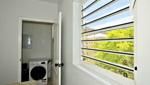 A laundry room with a washing machine, a dryer, and a window with horizontal blinds. - Westpunt Villa  l 2BR Near Turtle Beach (Westpunt)