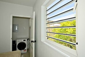 Ein Waschraum mit einer Waschmaschine, einem Trockner und einem Fenster mit horizontalen Jalousien.