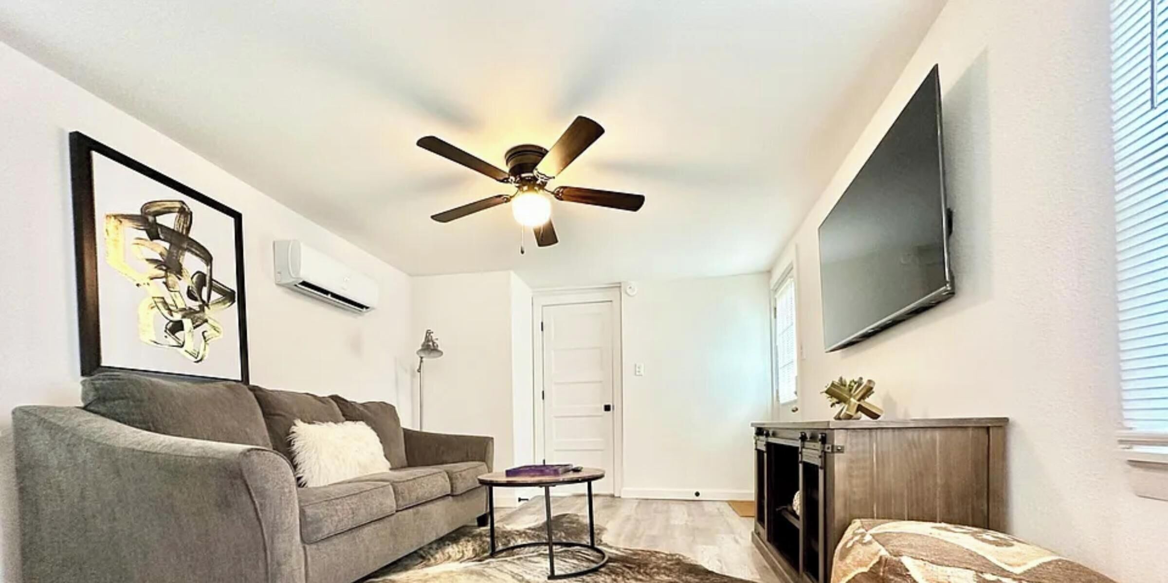 A living room with a ceiling fan, a sofa, a coffee table, a fireplace, and a mounted TV.