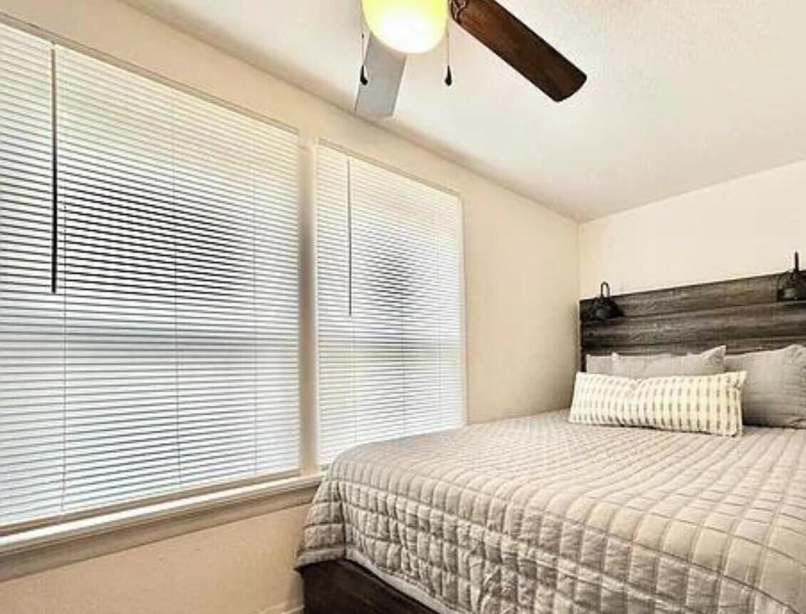 A bedroom with a bed, a ceiling fan, and two windows with blinds.