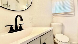 Et badeværelse med en hvid vask, sort armatur og et toilet.