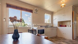 A kitchen with a dining table, a vase with flowers, a stove, and cabinets. - Classic 3 Bedroom Holiday Home (Twizel)