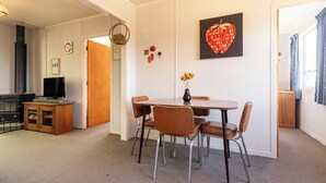A dining area with a table, chairs, a vase with flowers, a clock, and a television. - Classic 3 Bedroom Holiday Home (Twizel)