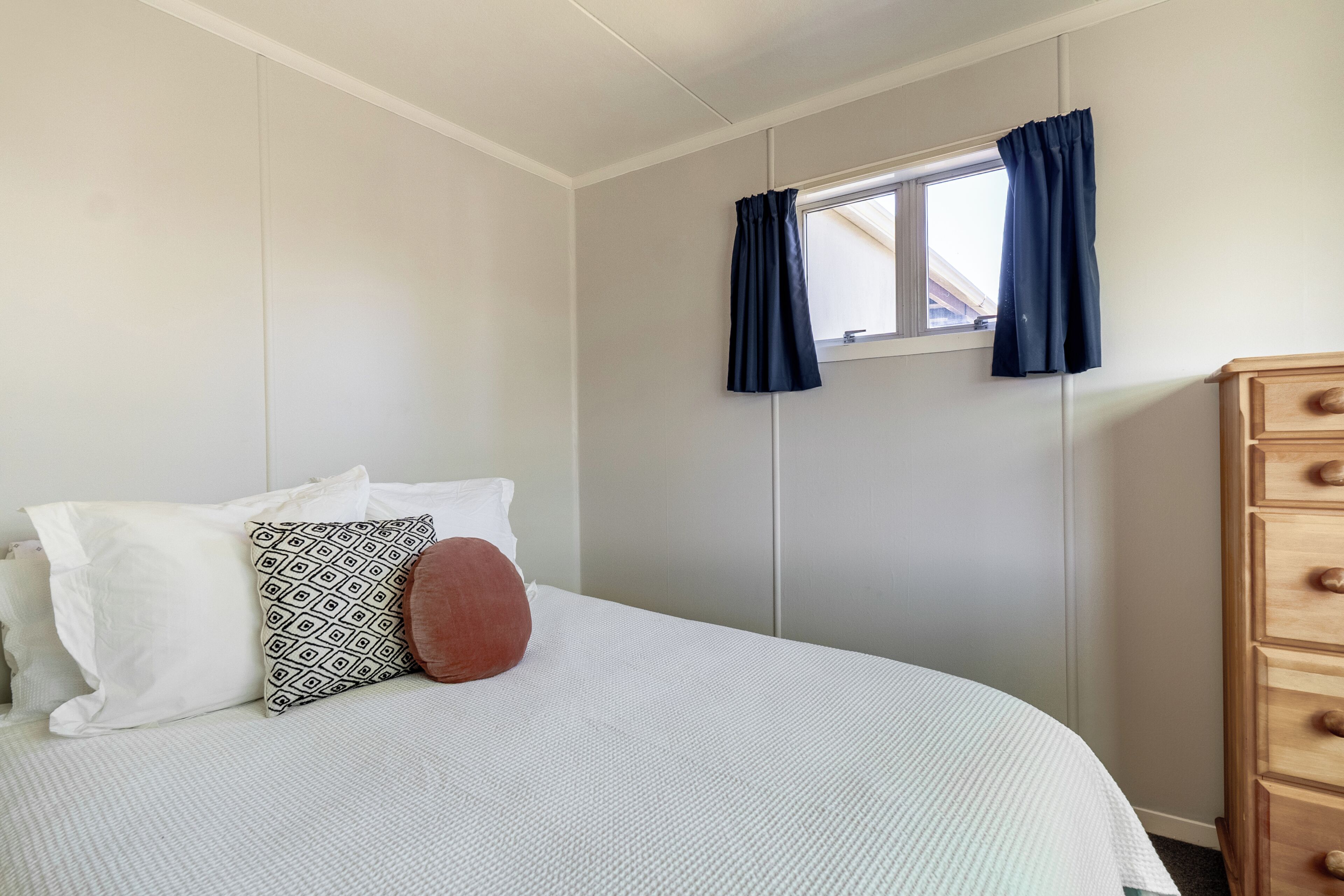 Une chambre à coucher avec un lit, une commode, une fenêtre avec des rideaux et un mur avec une fenêtre.