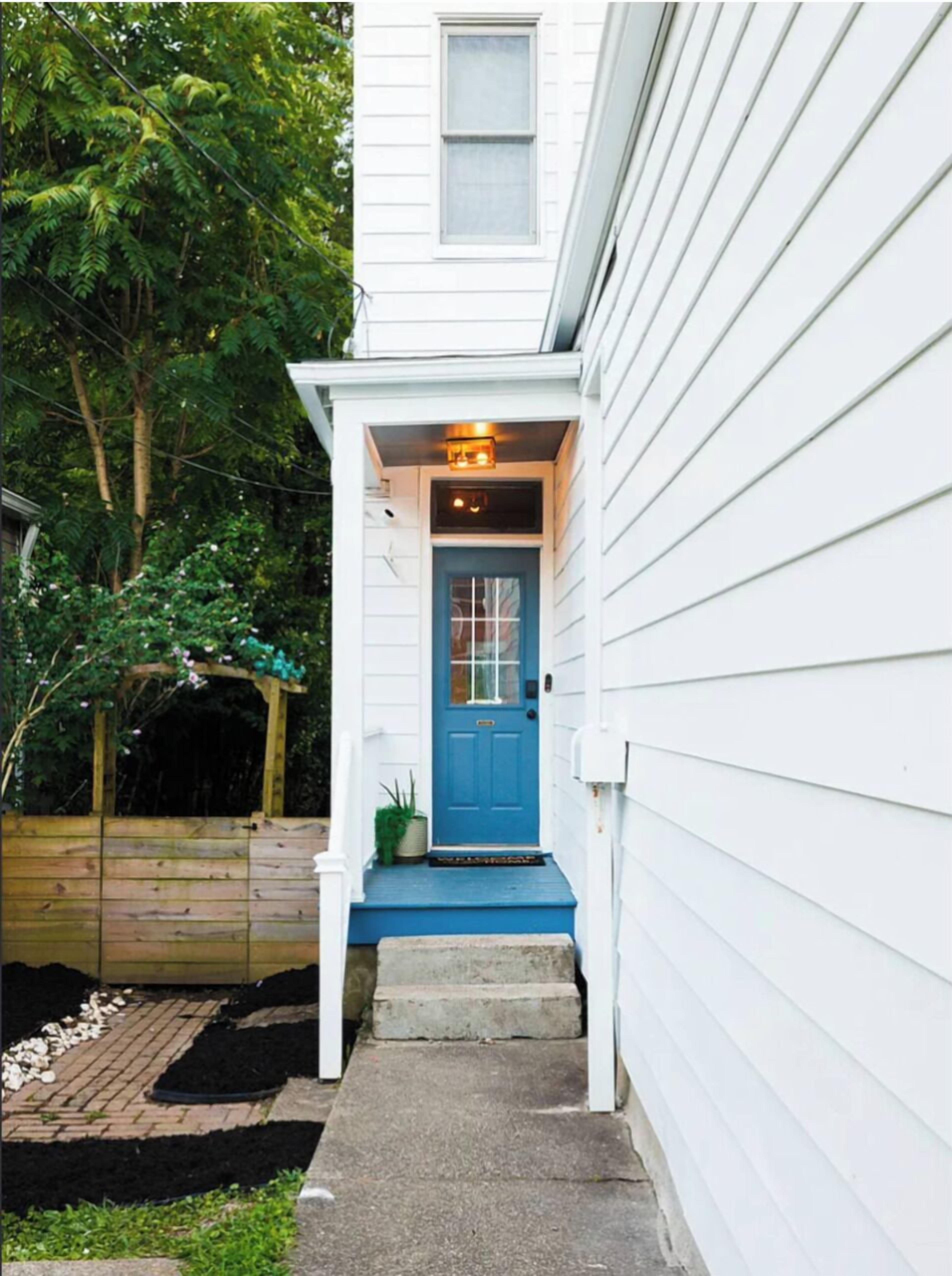Un bâtiment blanc avec une porte bleue, un petit porche et une clôture en bois.