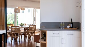 Una cocina moderna con sillas de madera, una mesa de comedor, luces colgantes y una botella de vino sobre la encimera.