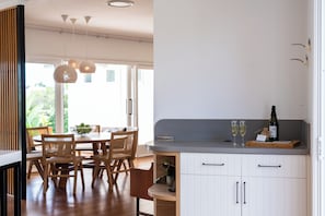 Eine moderne Küche mit Holzkästen, einem Esstisch, Pendelleuchten und einer Weinflasche auf der Arbeitsplatte.