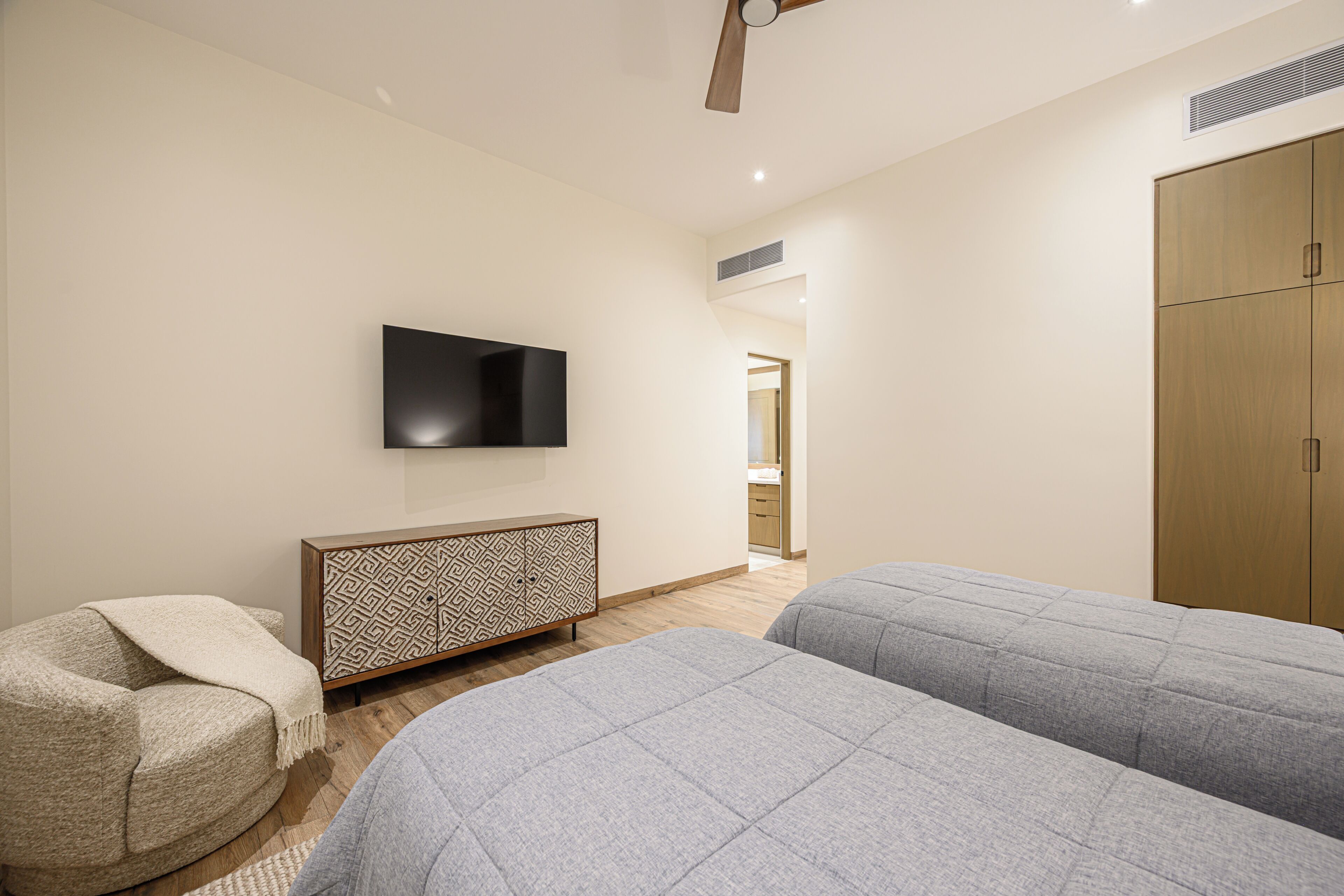 A bedroom with two beds, a TV, a wardrobe, and a ceiling fan.