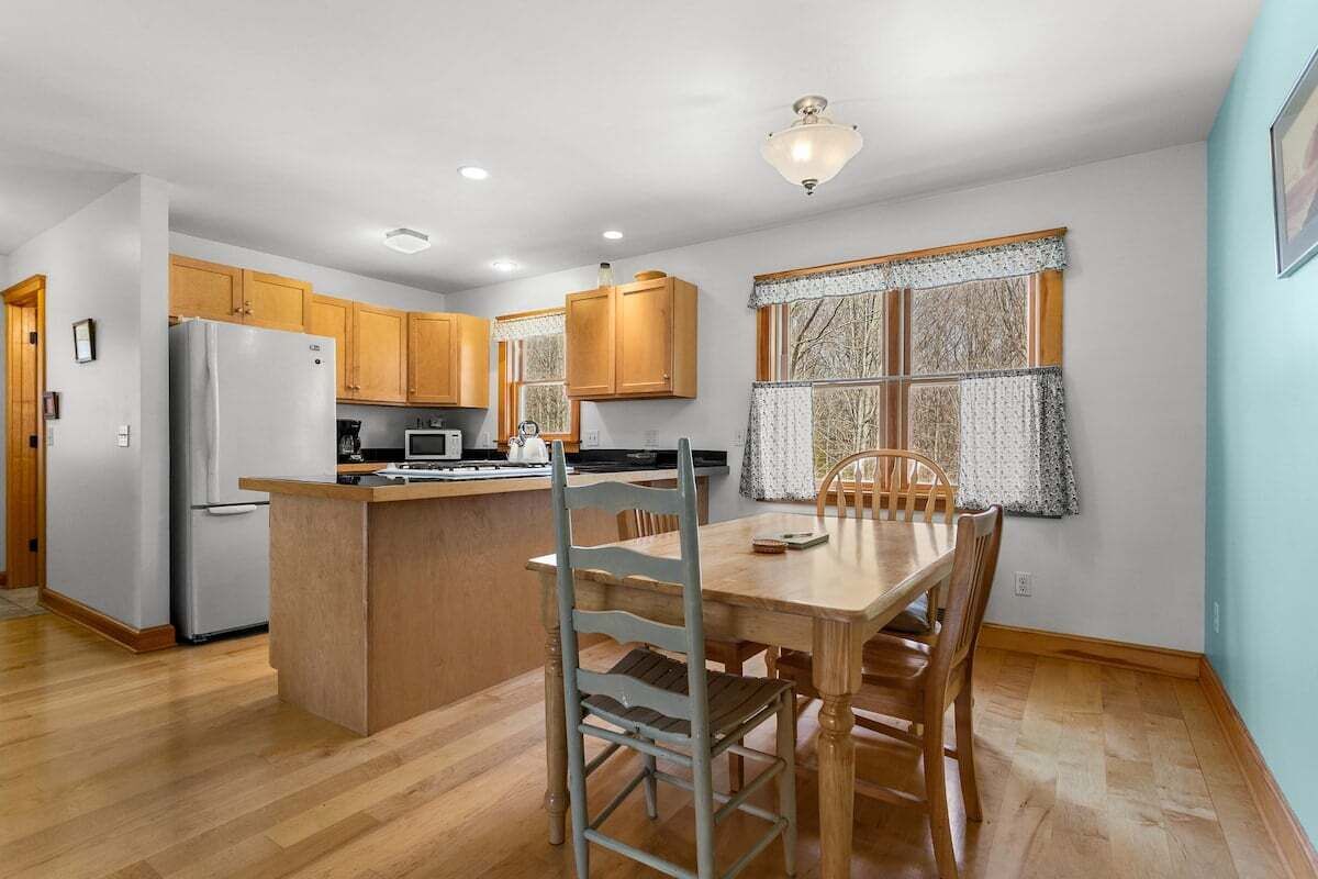 A kitchen with wooden cabinets, a refrigerator, a microwave, and a dining table with chairs.