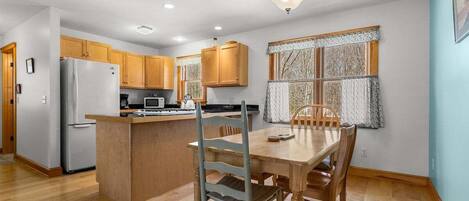 A kitchen with wooden cabinets, a refrigerator, a microwave, and a dining table with chairs.