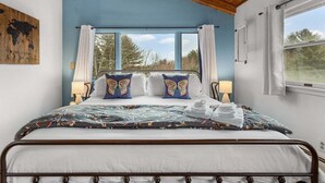 Un dormitorio con una cama, dos lámparas de noche, un ventanal con cortinas y techo de madera.