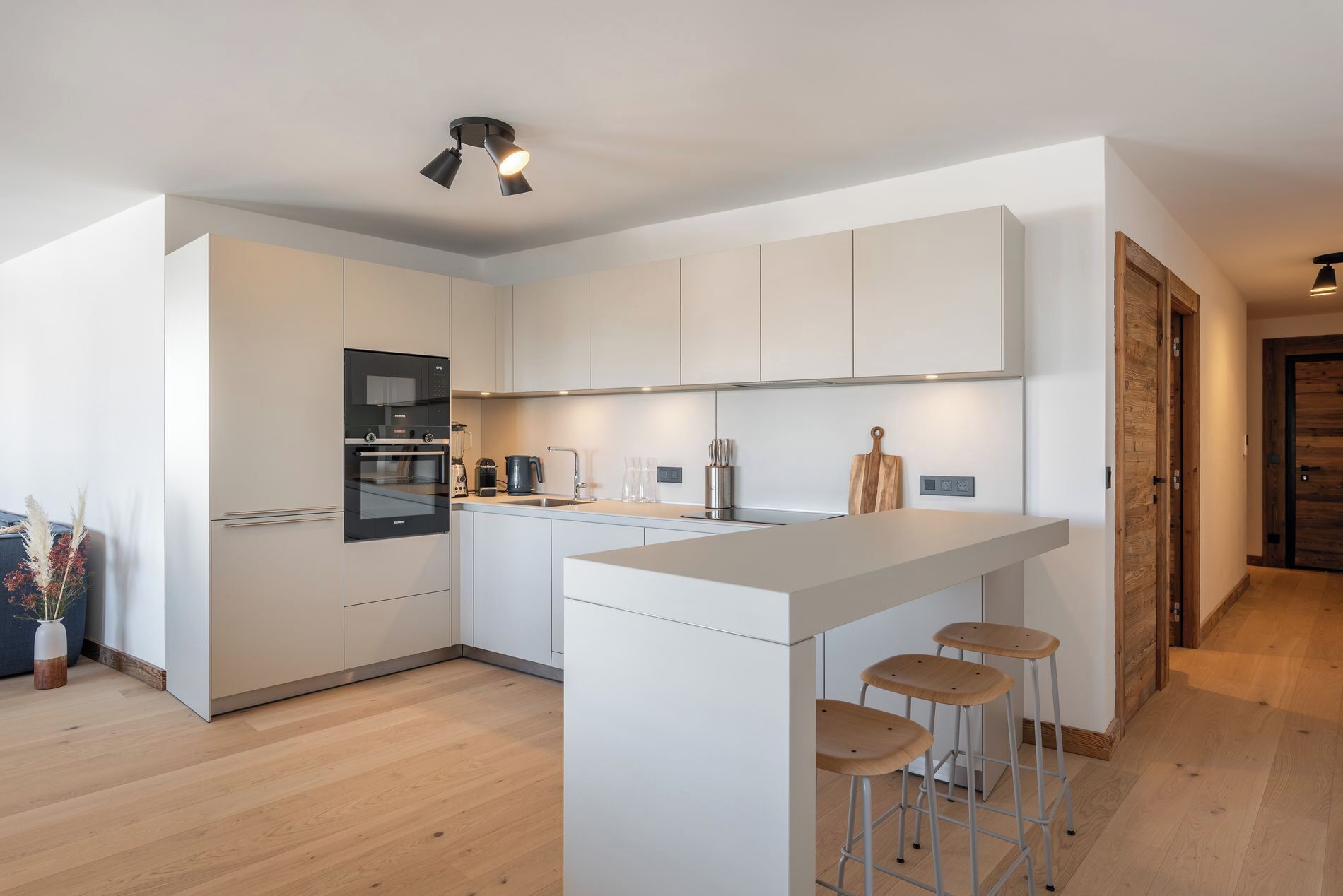 Een moderne keuken met witte kastjes, een inbouwoven, een koffiezetapparaat en een houten snijplank.