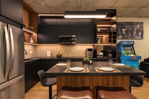 A modern kitchen with a central island, built-in appliances, and a retro arcade machine. - UNA Torre (Monterrey)