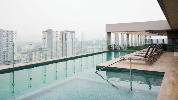 Una piscina infinita en la azotea con vistas a la ciudad, sillas de descanso y un diseño arquitectónico moderno.
