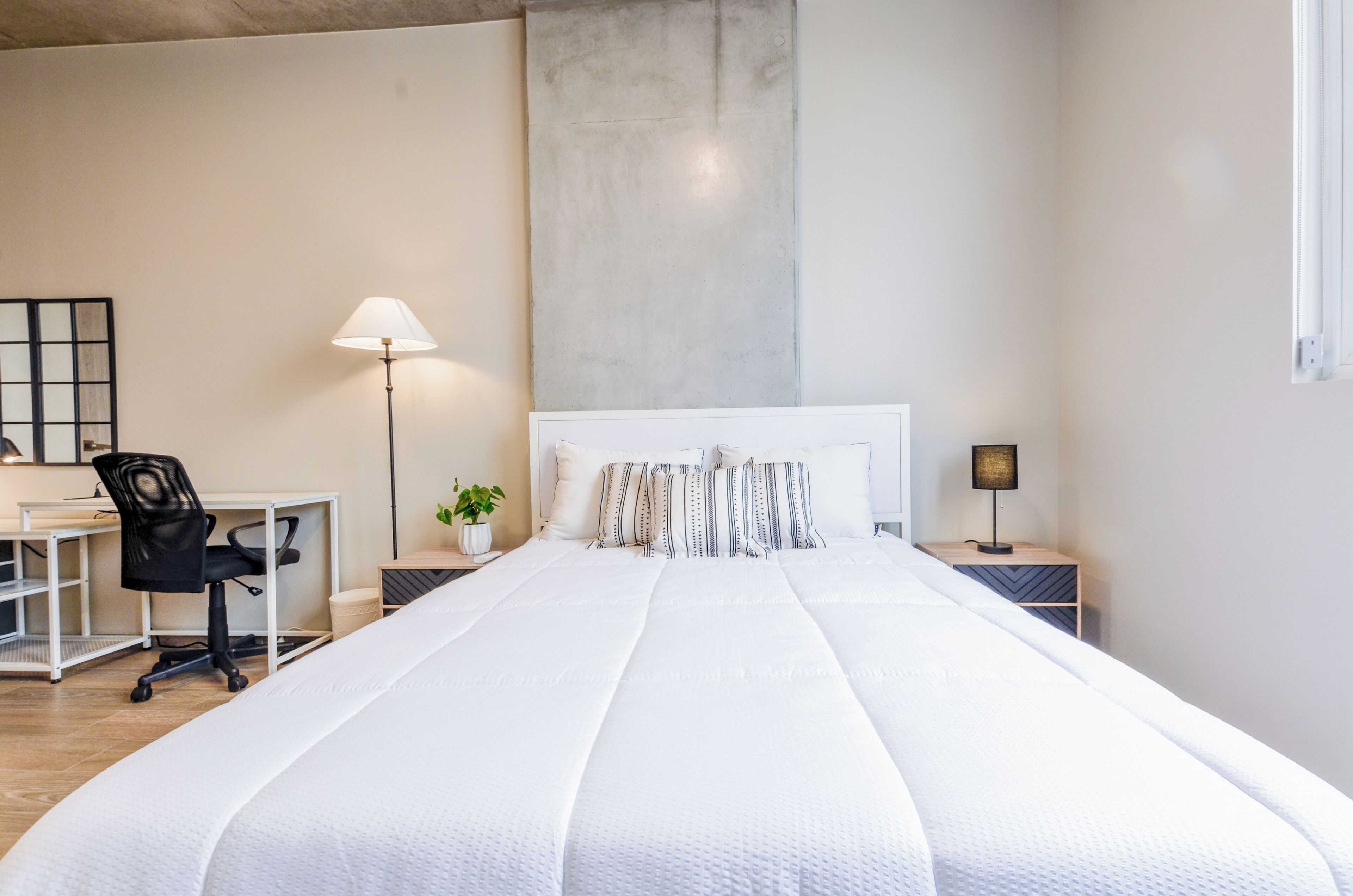 A bedroom with a large bed, a desk, a chair, two nightstands, and a lamp.
