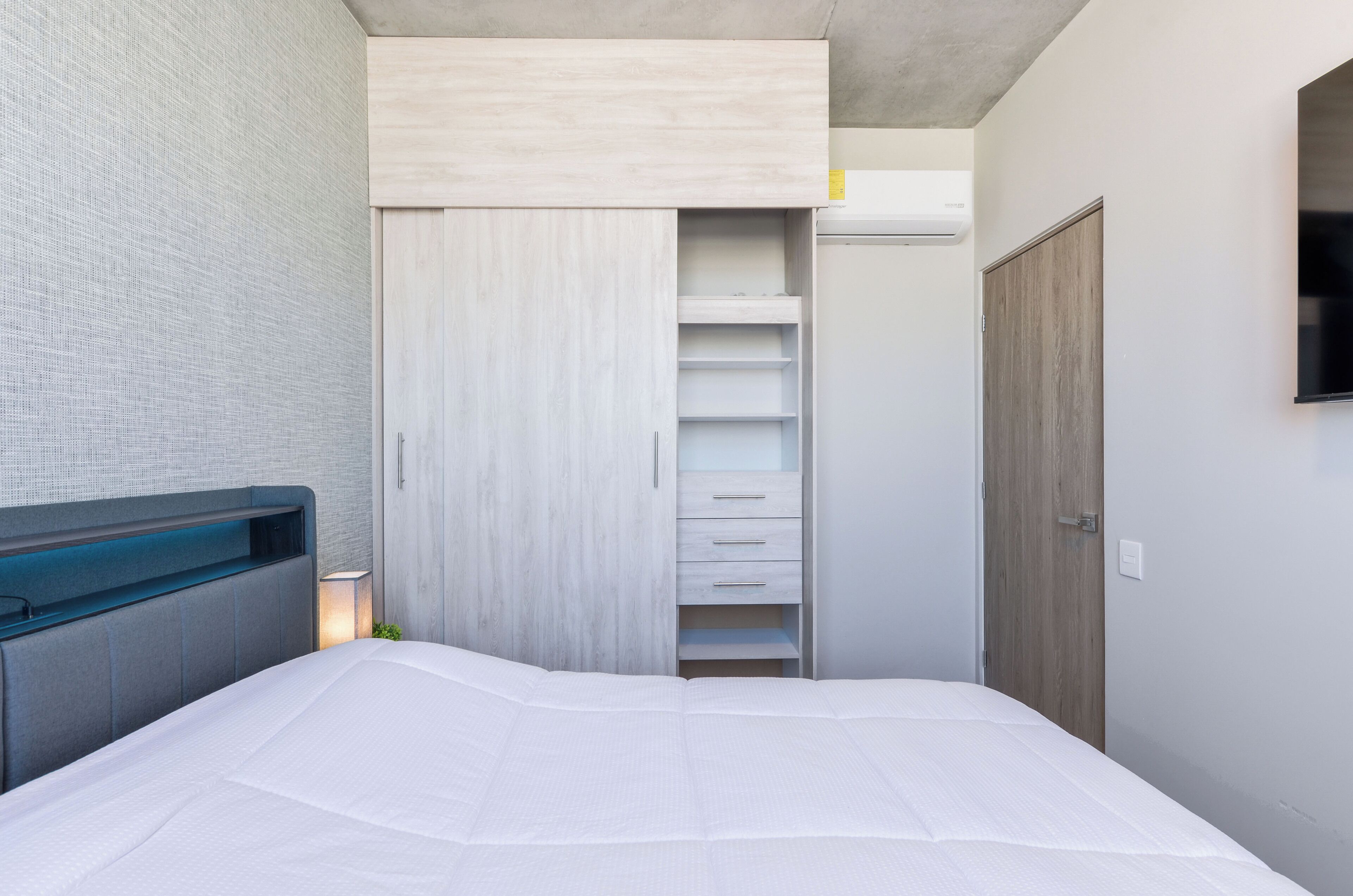 Een slaapkamer met een bed, een kledingkast, een nachtkastje en een aan de muur bevestigde televisie.