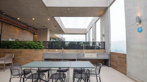 Un espacio de comedor al aire libre con mesa y sillas, una estación de parrilla y vistas de la ciudad.