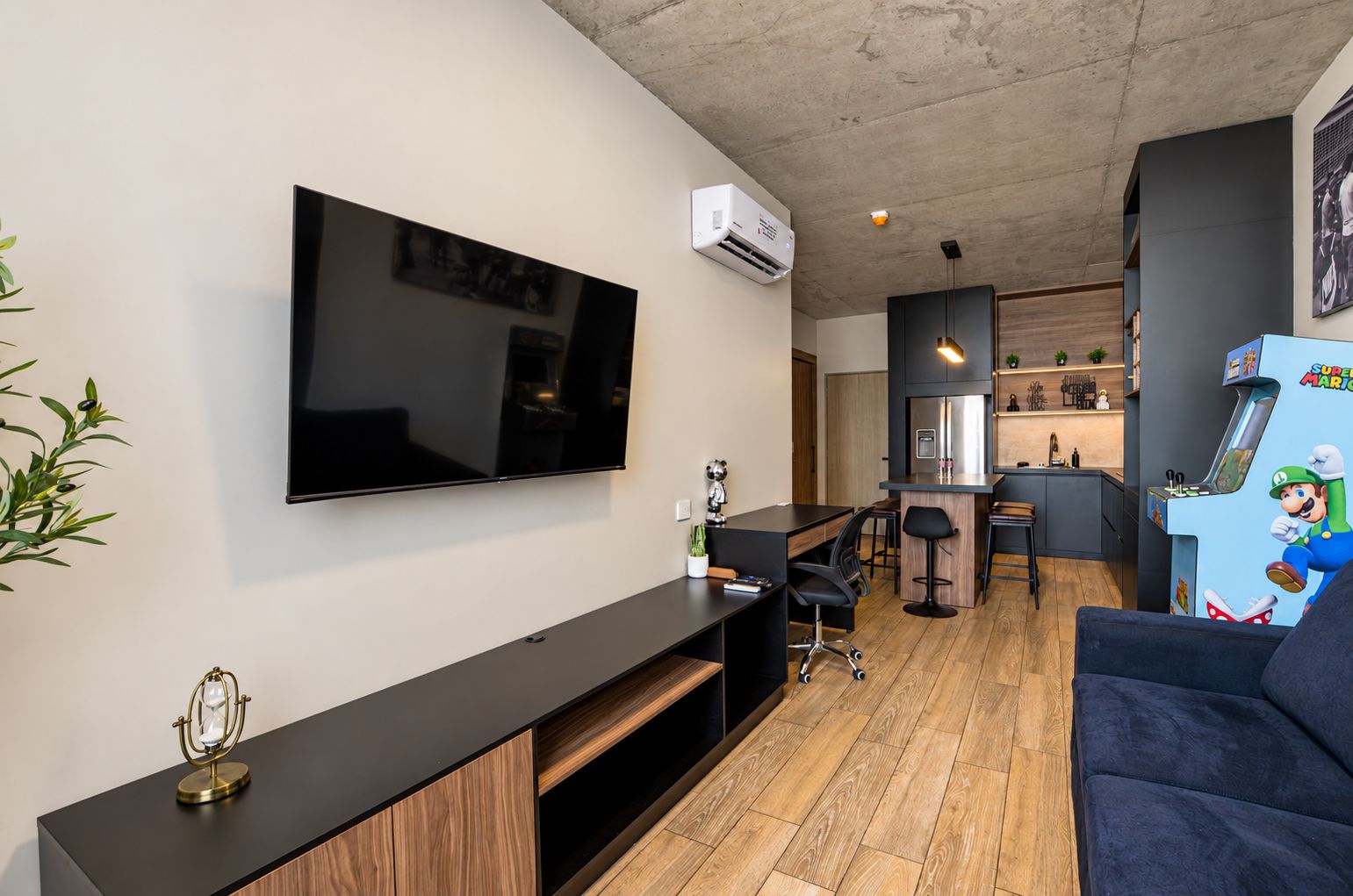 A modern living room with a flat-screen TV, a kitchen area, and a Mario-themed arcade machine.