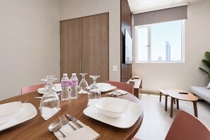 A dining area with a wooden table set for four, including plates, cutlery, and glasses. - UNA Torre (Monterrey)