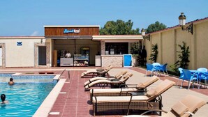 Zona de piscina con sillas de descanso, un bar y un letrero que dice 'Jungle Inn'.