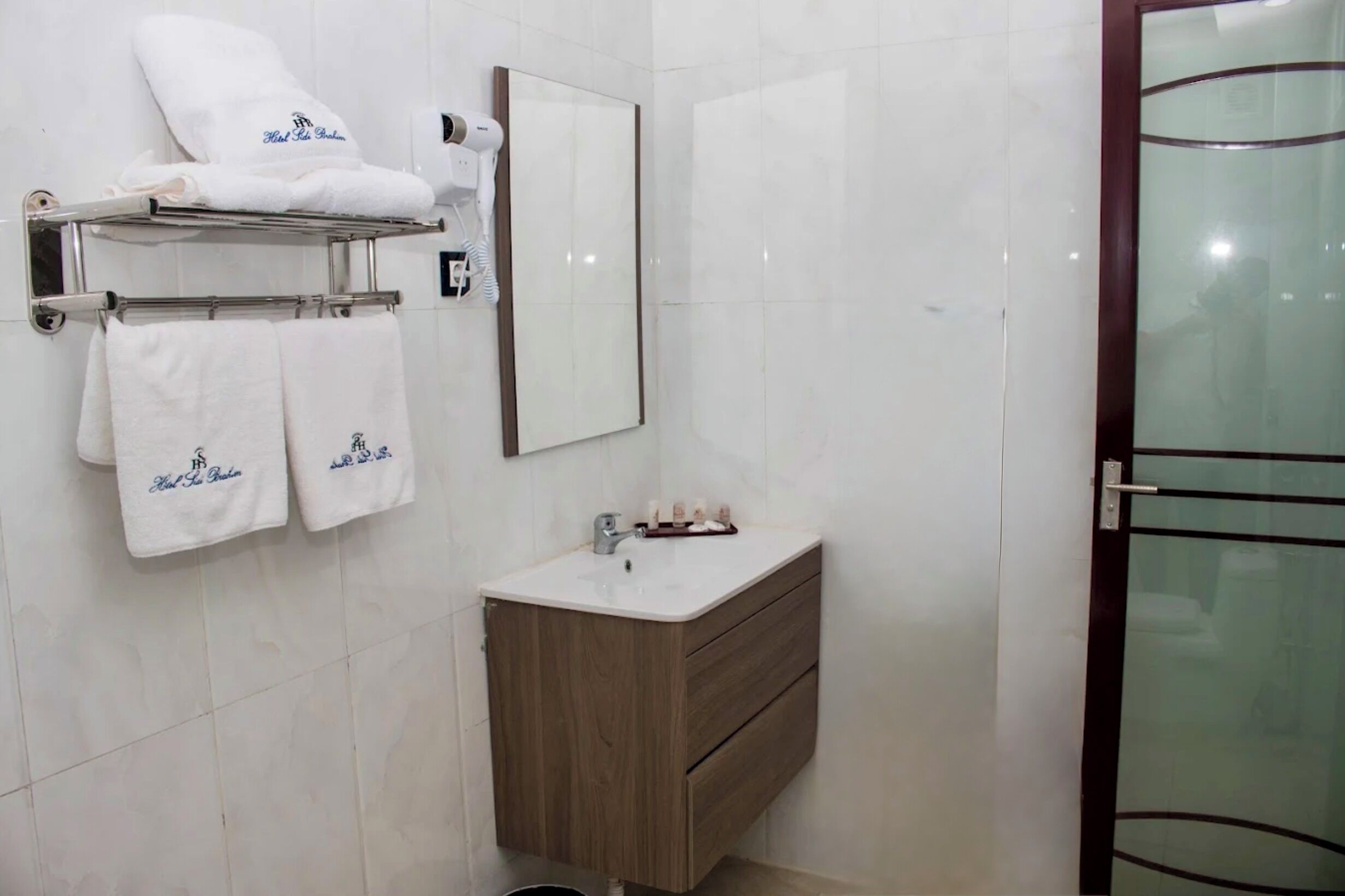 A bathroom with a mirror, a sink, a towel rack with towels, and a glass shower door.
