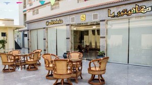 Un café con mobiliario de mimbre en el exterior, una escalera y la entrada de un edificio.
