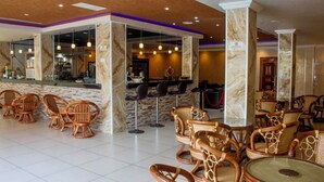 Un vestíbulo de hotel con sillones de mimbre, una zona de bar y columnas de mármol.