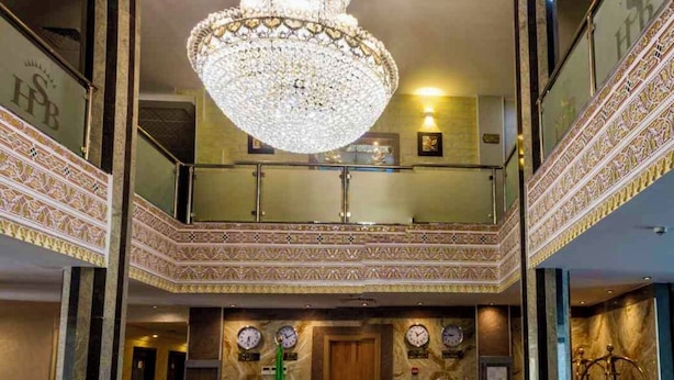 Vestíbulo de hotel con una gran lámpara de araña, mostrador de recepción y un balcón de doble altura con detalles intrincados.