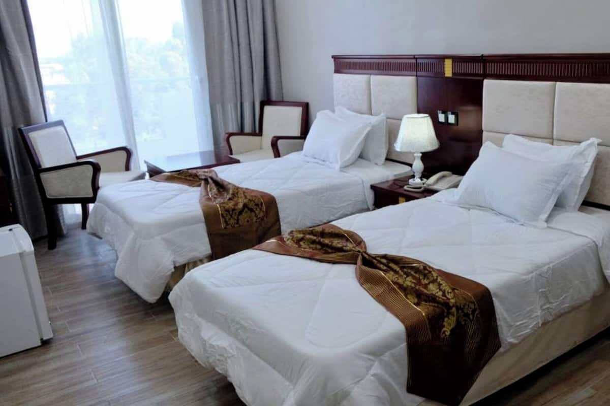Habitación de hotel con dos camas, una mesita de noche con lámpara, una silla y un escritorio con teléfono.
