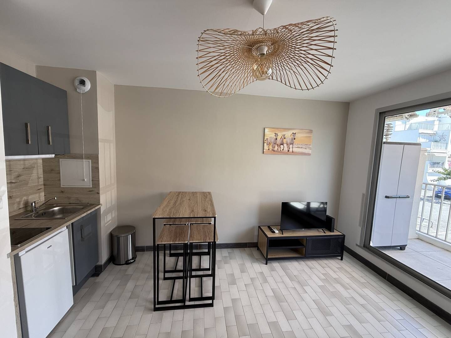 A modern kitchen with a wooden countertop, a black metal chair, a TV on a wooden stand, and a large window with a view of buildings.