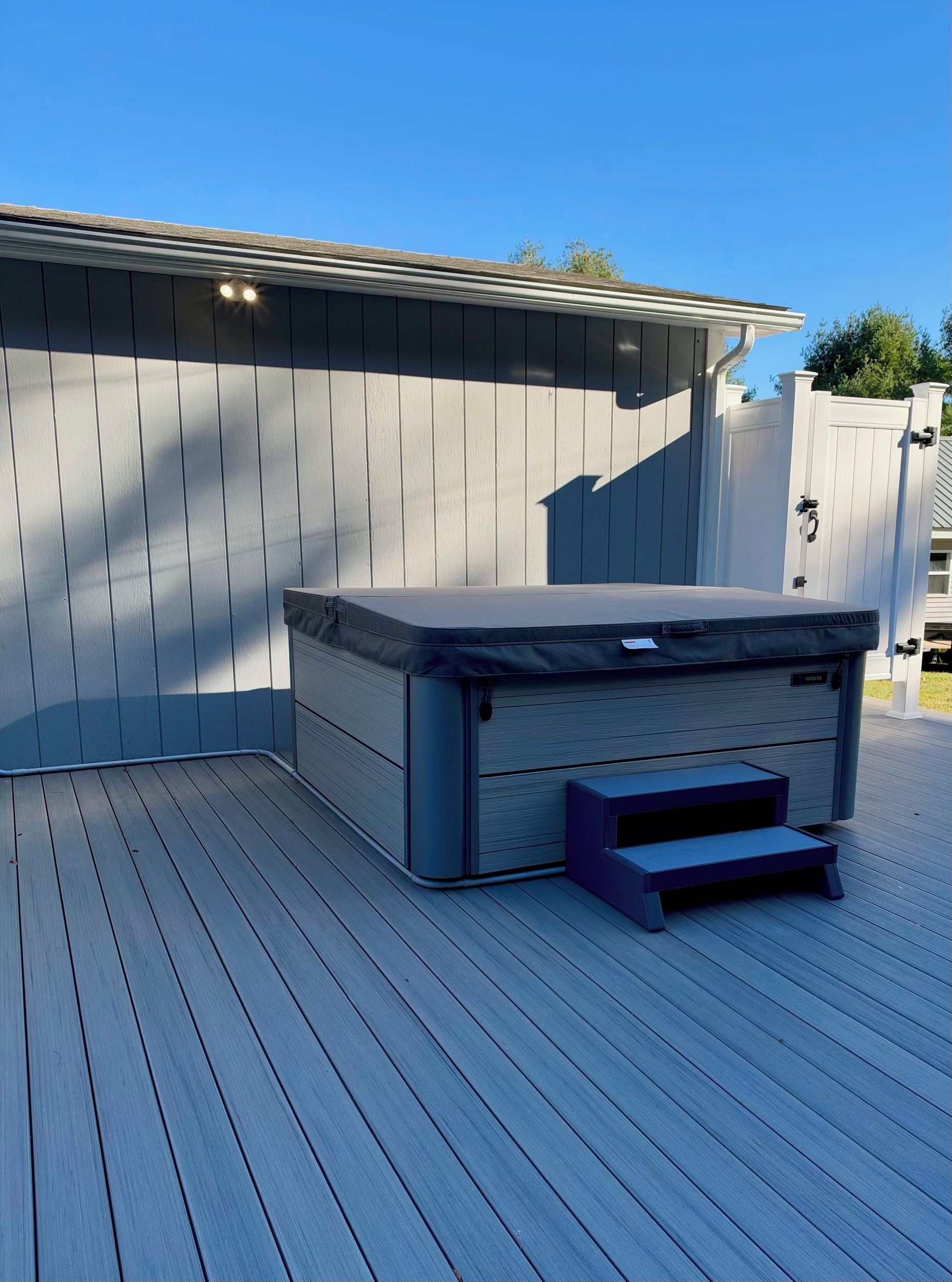 A hot tub on a wooden deck with a white fence in the background.